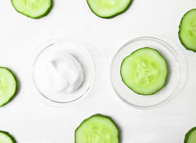 Gurkenscheiben um einen Behälter mit weißer Creme auf hellem Hintergrund.