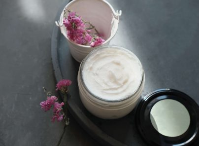 Hautpflegecreme in einem Glas mit getrockneten Blumen und leerem Behälter auf einem Tisch.