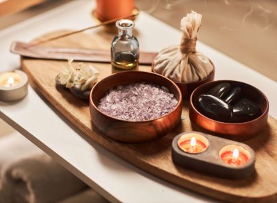 Aromatische Wellness-Dekoration mit Steinen, Salz, Kräutern und Kerzen auf einem Holzbrett.