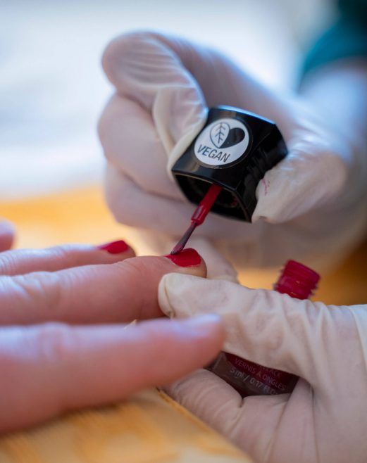 Veganer Nagellack wird auf eine Hand mit rotem Nagellack aufgetragen.