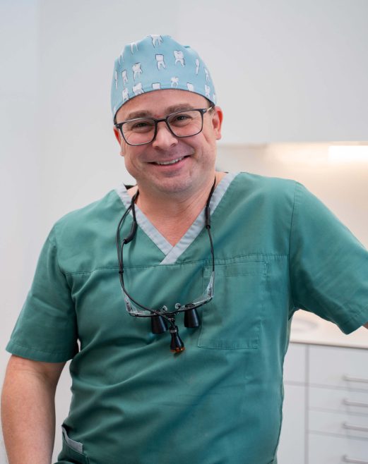 Zahnarzt in Praxismitarbeiterkleidung lächelt, bereit für Patienten im Gesundheitszentrum Radstadt.