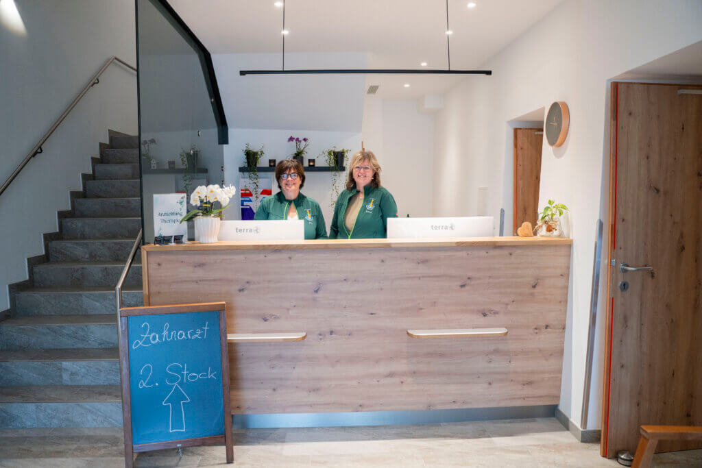 Empfangsbereich im Gesundheitszentrum Radstadt mit lächelnden Mitarbeiterinnen und Treppe.