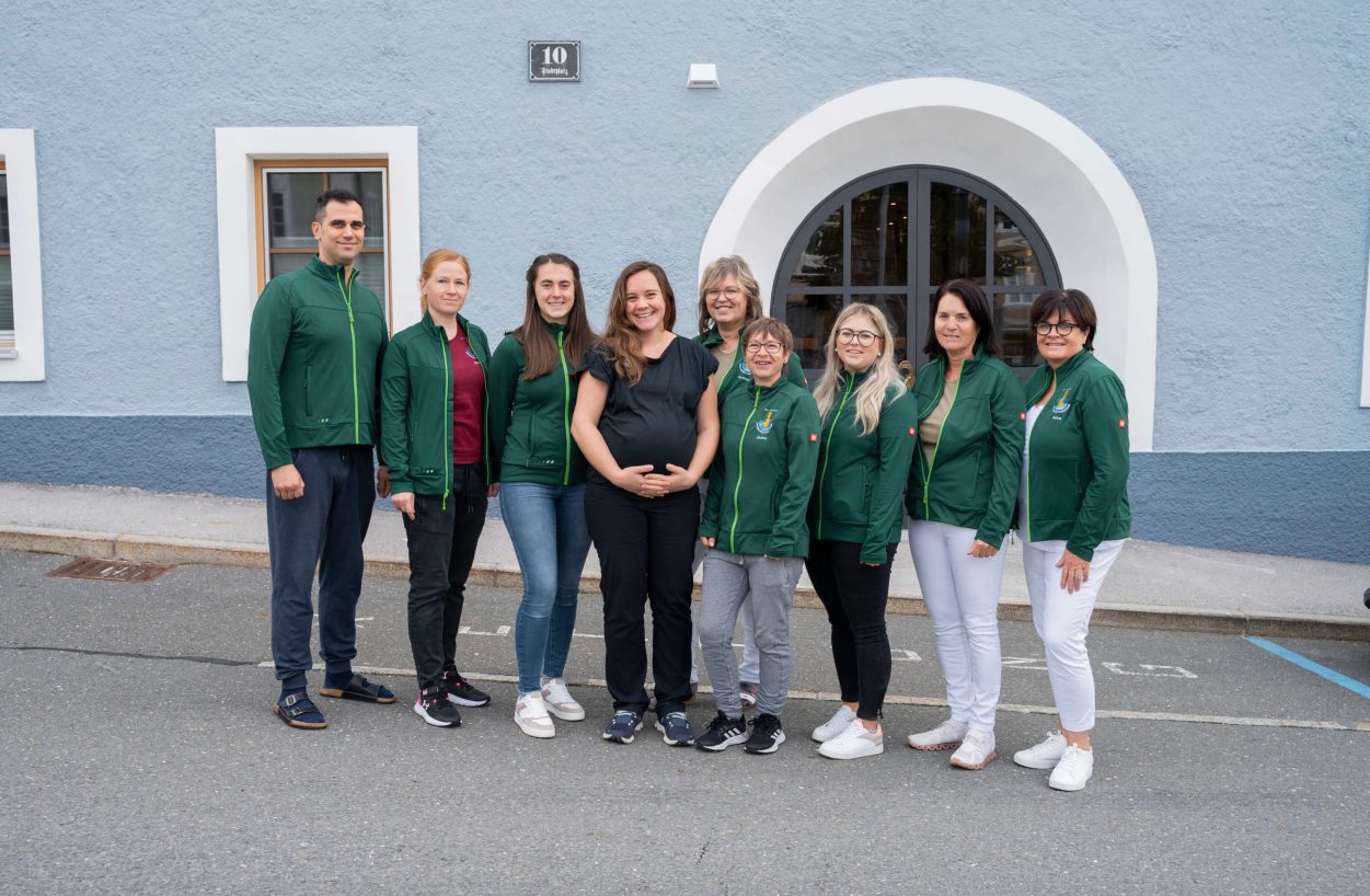 Team des Gesundheitszentrums Radstadt vor der Praxis, in grünen Jacken versammelt.